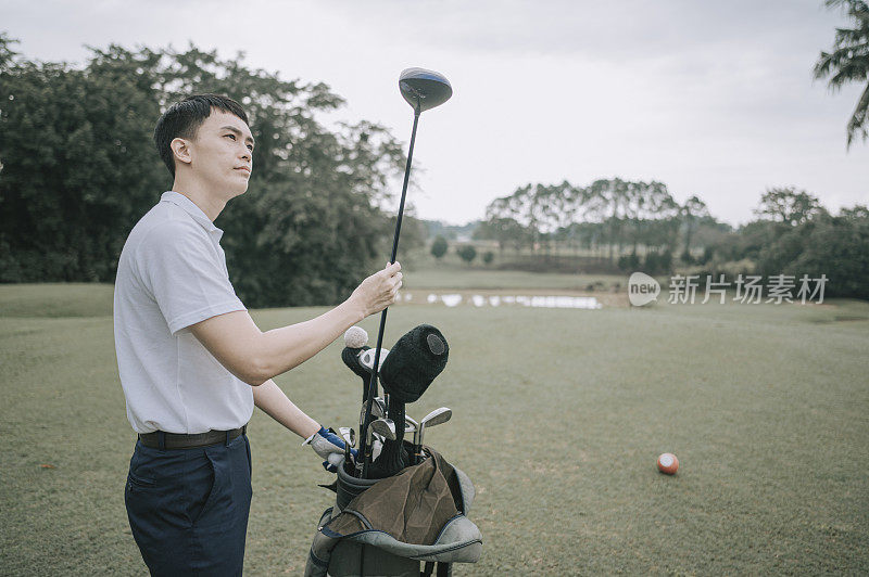 Asian chinese male golfer selecting driver golf club from golf bag for tee off at the golf course tee off point